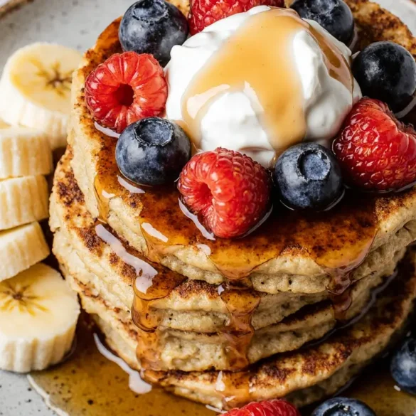 cottage cheese banana pancakes A close-up of a delicious stack of cottage cheese banana pancakes, topped with fresh berries, yogurt, and maple syrup.